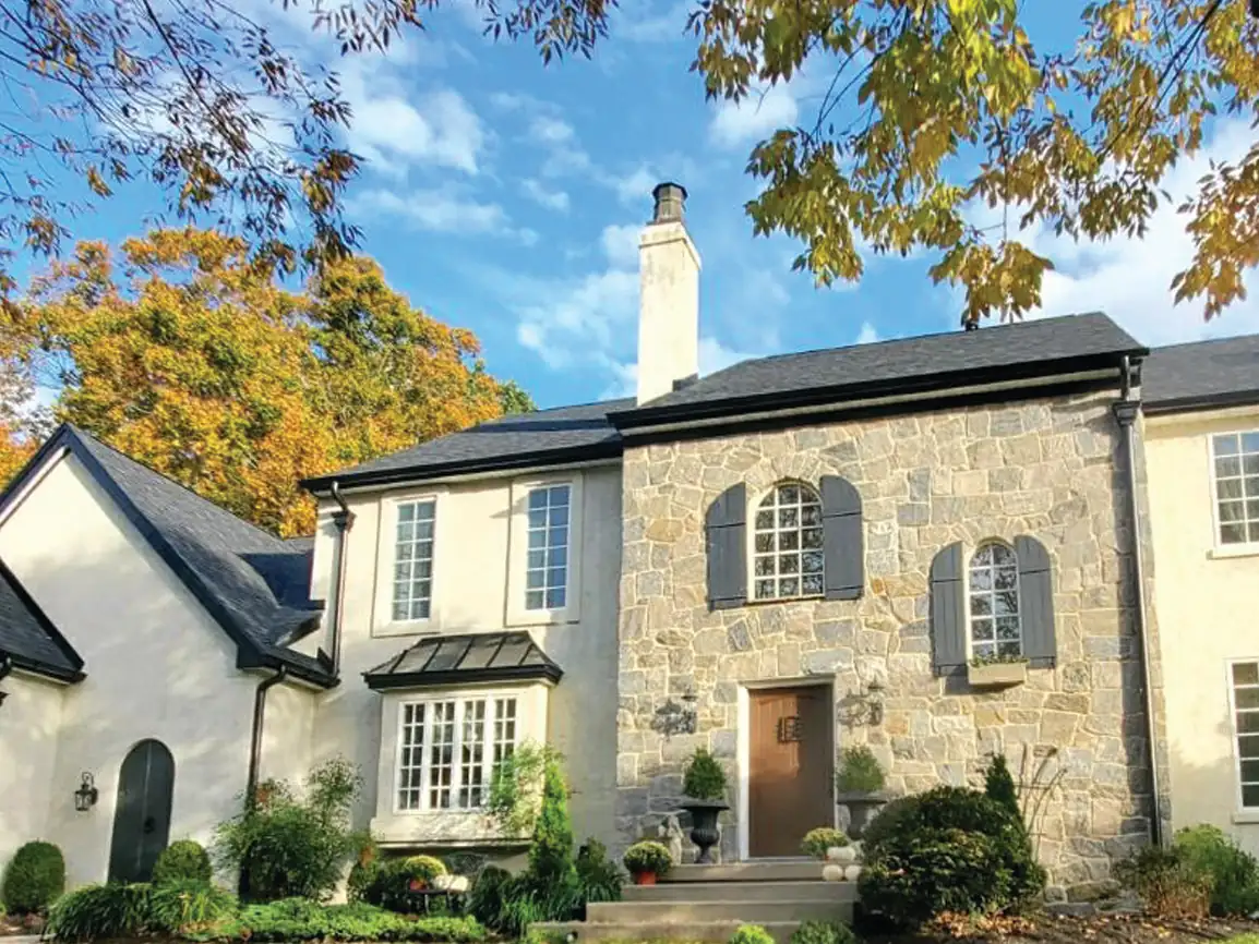A stone and stucco two-storey house with arched windows and dark shutters, a wood front door, and a tall white chimney.