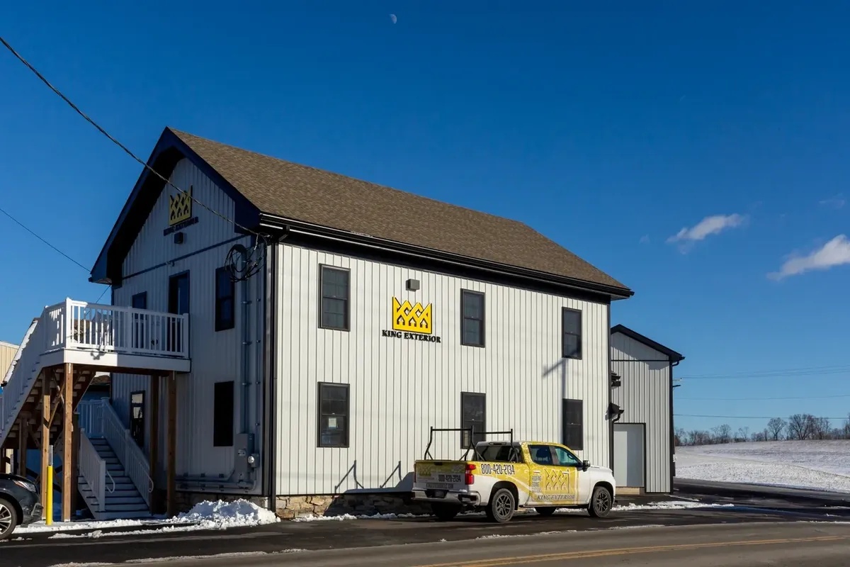 Two-story white board-and-batten commercial building with a wrapped contractor pickup truck parked outside on a clear winter day.
