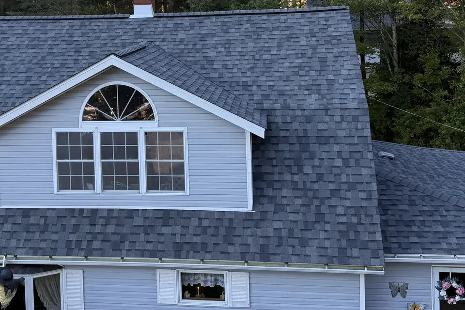 A gambrel roof covered in new gray architectural shingles, with a white arched dormer window set into the slope.