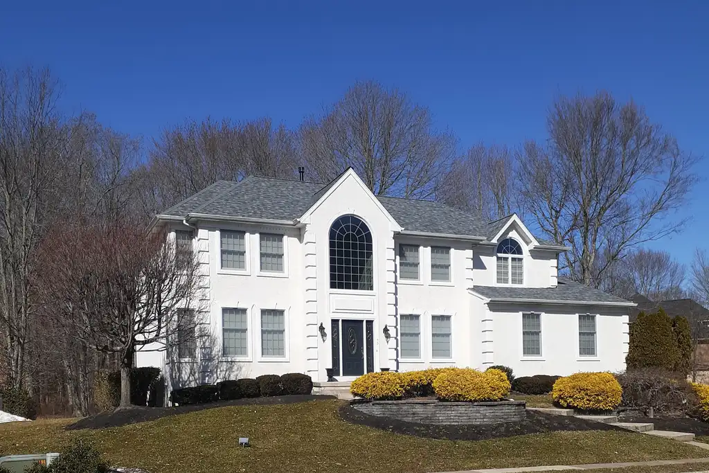 A white two-storey colonial house with a grey asphalt shingle roof and an arched front window, seen from the street on a clear winter day.