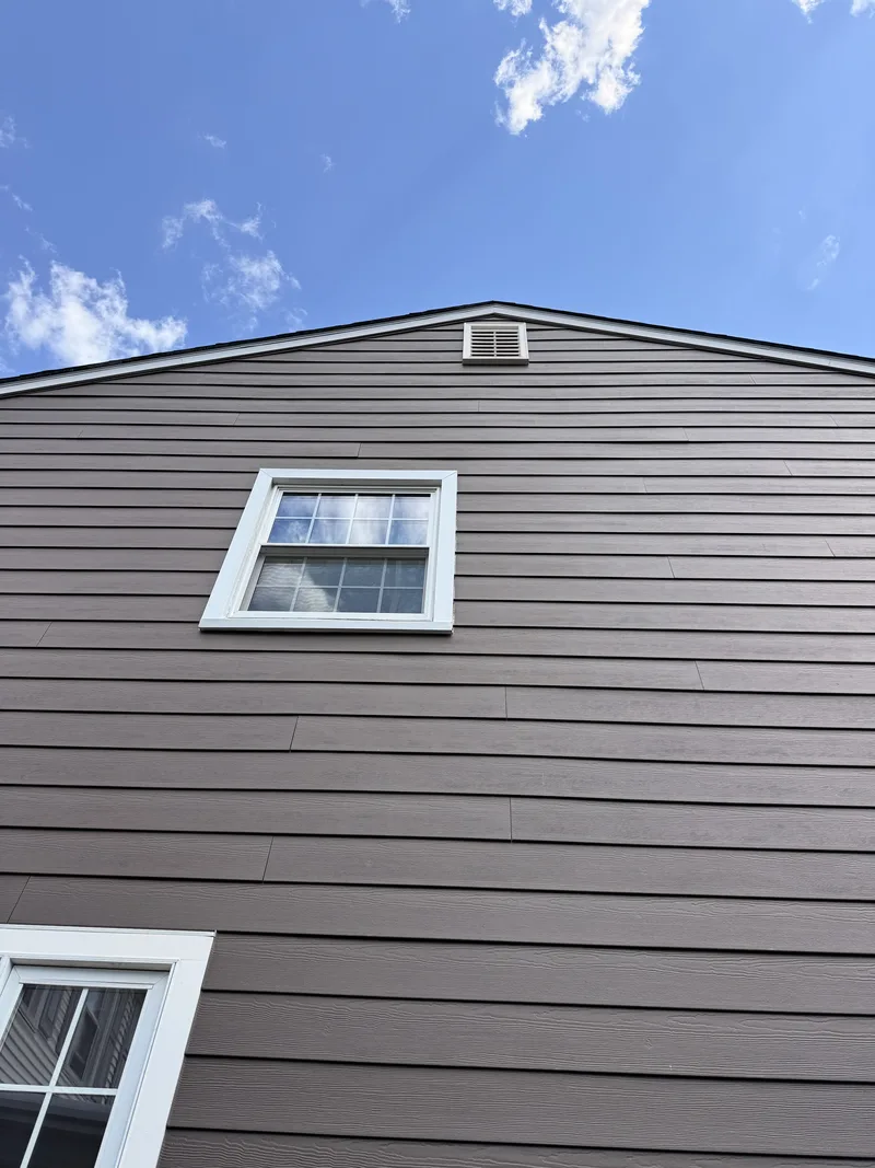 Mocha horizontal lap siding with a wood-grain texture running up to a gable end, around a white-trimmed window.